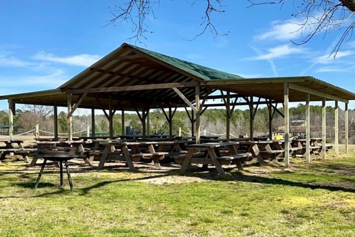Open pavilion with picnic tables on a grassy area under a blue sky.